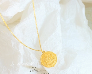 Macro shot of 18k gold plated vintage coin pendant with embossed crest on a fine chain