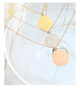Macro detail of three-tone coin necklaces with embossed crest on a textured glass
