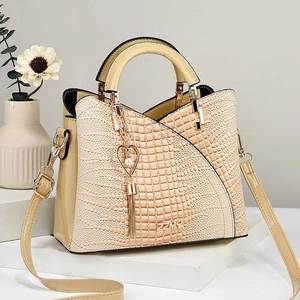 Detail der aprikosenfarbenen Handtasche mit Krokodilprägung und einem Herz-Perlenanhänger