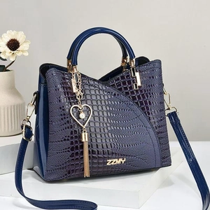 Dunkelblaue Handtasche mit Krokodilprägung und Herz-Perlenanhänger auf weißem Podest