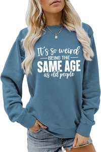Detail of blue crewneck sweatshirt with It's so weird BEING THE SAME AGE printed text