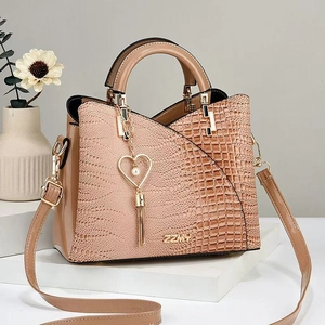 Detail der nudepinkfarbenen Handtasche mit Krokodil-Patchwork und Herz-Perlen-Anhänger