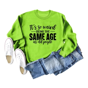 Flat lay of neon green sweatshirt with 'It's so weird' slogan and denim shorts
