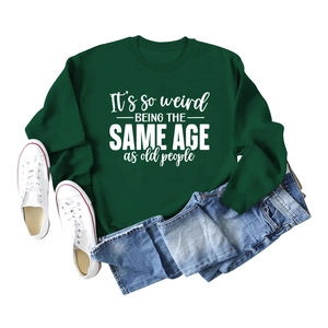 Flat lay of forest green sweatshirt with 'It's so weird' slogan and denim shorts