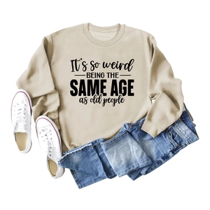 Close-up of beige crewneck sweatshirt with 'It's so weird' artistic print text