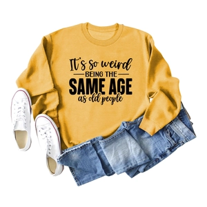 Flat lay of yellow long sleeve sweatshirt with 'It's so weird' slogan and blue jeans