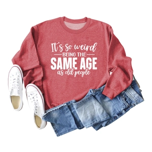 Close-up of red crewneck sweatshirt with white 'It's so weird' text flat lay display