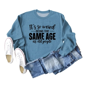 Flat lay of blue sweatshirt with 'It's so weird' text, denim shorts and white sneakers