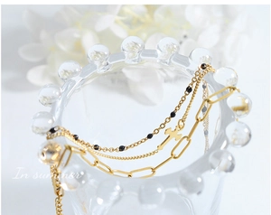 Close-up of triple-layered gold bracelet featuring cross pendant and paperclip chain