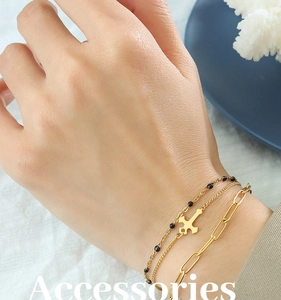 Detail of layered gold paperclip chain bracelet with cross pendant and black beads