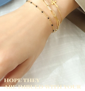 Detailed shot of layered 18k gold plated chains with cross pendant and black beads
