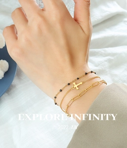 Detailed view of triple-layered gold bracelet featuring cross pendant and paperclip chain