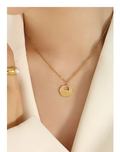 Gros plan d'un collier pendentif cadenas Ruyi doré porté avec un blazer crème
