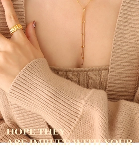 Detail of gold fringe necklace and textured wave ring paired with knit sweater