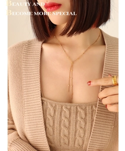 Detail of gold Y-shaped tassel necklace and textured wave ring on model's neck