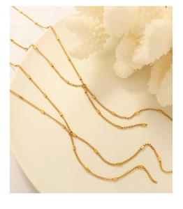 Macro shot of minimalist gold tassel necklace with cylindrical tube beads on fine chain