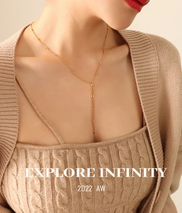 Detail of long gold-plated Y-shaped tassel necklace on a beige knit sweater model