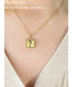 Détail d'un collier pendentif carré doré avec visage abstrait porté sur un mannequin