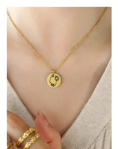 Détail du collier à pendentif rond doré avec gravure minimaliste d'un visage abstrait