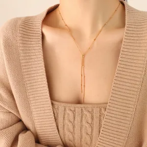 Elegant gold-tone Y-shaped tassel necklace with cylinder charms on a minimalist model