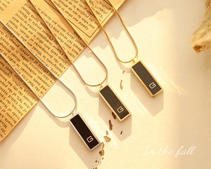 Close-up of a minimalist black acrylic G-pendant on a gold snake chain necklace