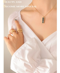 Detail of gold chain necklace with black rectangular G-pendant and textured gold rings
