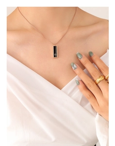 Detailed close-up of rose gold necklace with black acrylic G tag and quilted ring