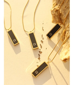 Macro detail of gold plated snake chains with black G pendant on a textured stone surface