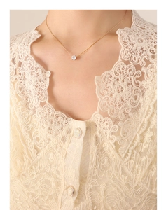 Close-up of a minimalist gold zircon solitaire necklace worn on a beige lace garment