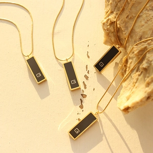 Gold plated snake chain necklace with black acrylic rectangular G pendant on stone