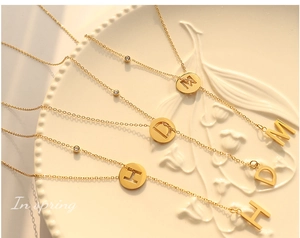 Detail of three gold Y-shaped necklaces with MHD letter charms and zircon on ceramic plate