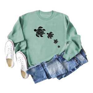 Close-up of light green sweatshirt featuring four black sea turtle prints and ribbed cuffs
