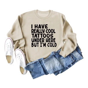 Flat lay of a beige slogan sweatshirt with I Have Really Cool Tattoos text and jeans