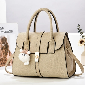 Sac fourre-tout tissé beige avec fermoir doré et pendentif peluche sur une table