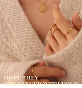 Detail showing irregular molten texture gold pendant and stacked minimalist rings on knitwear