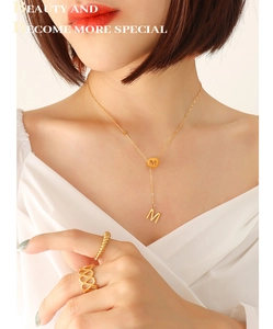 Detail of 18k gold plated Y-shaped tassel necklace with M letter and matching gold rings