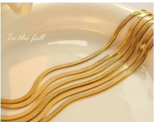 Macro detail of high-polish gold flat snake chain necklace set with woven texture