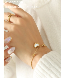Detail of a gold heart bracelet with white shell inlay and a matching link ring
