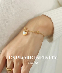 Detail of a gold-plated heart pendant bracelet with shell inlay on white knit sweater