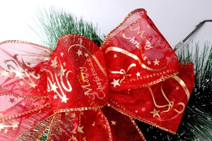 Detail van rode kerststrik met gouden Merry Christmas-belettering en groene dennennaalden