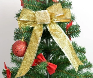 Close-up of a sparkling gold glitter bow ornament placed on a decorated Christmas tree