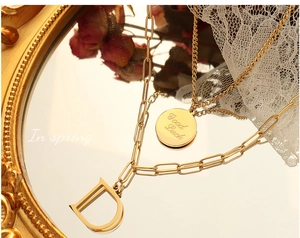 Detalle del collar de doble capa chapado en oro de 18K con colgantes de letra D y Good Luck