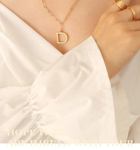 Detalle del collar con colgante letra D bañado en oro 18K y anillos con relieve