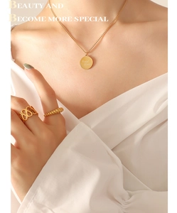 Primer plano de collar chapado en oro 18K con colgante Good Luck y anillos en modelo