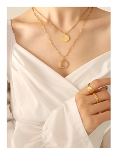 Detalle del collar dorado de capas con colgante D y anillos texturizados en modelo