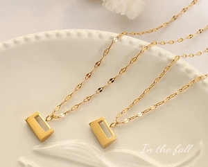 Close-up of golden rectangular cutout pendants on elegant twisted chain necklaces
