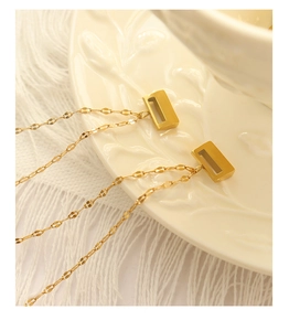 Detailed close-up of a gold-plated rectangle pendant necklace on a decorative ceramic plate