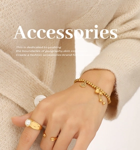 Detail von 18K vergoldetem Perlenarmband mit Fu-Anhänger und passenden Ringen auf Strickware