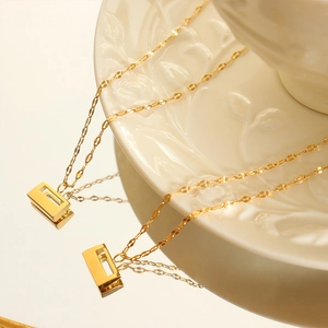 Minimalist 18K gold plated titanium necklace with rectangular geometric pendant on a plate
