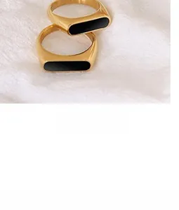Detail of minimalist gold-tone rectangular ring featuring black enamel inlay on fabric